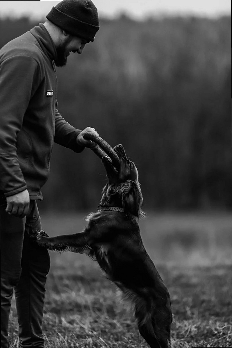 A man playing with his pet dog in a meadow, captured in black and white.
